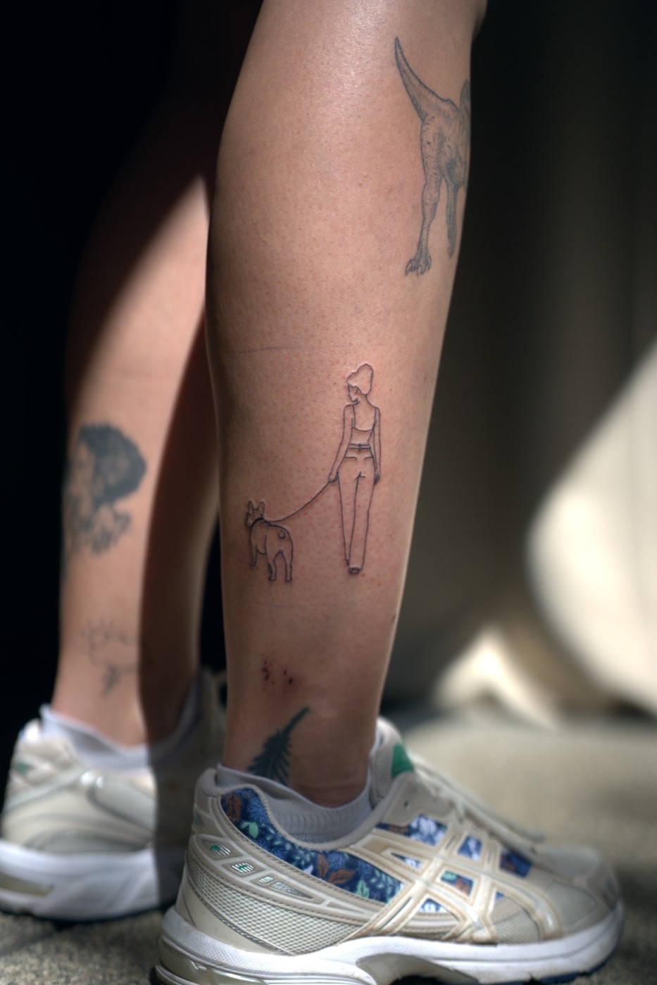 Tatouage fine line d'une femme promenant son chien, mollet